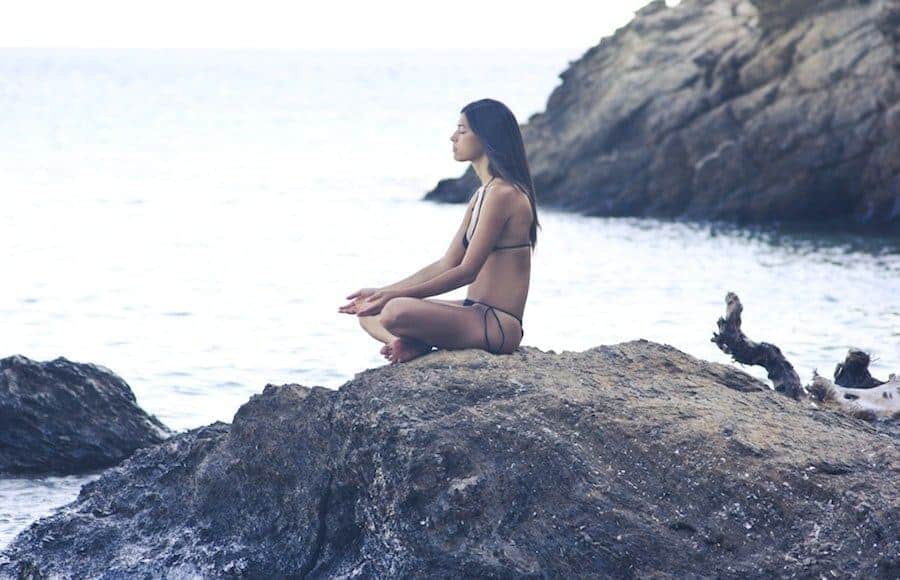 Brunette girl in bikini meditating on a beach in Bali | flystayluxe.com
