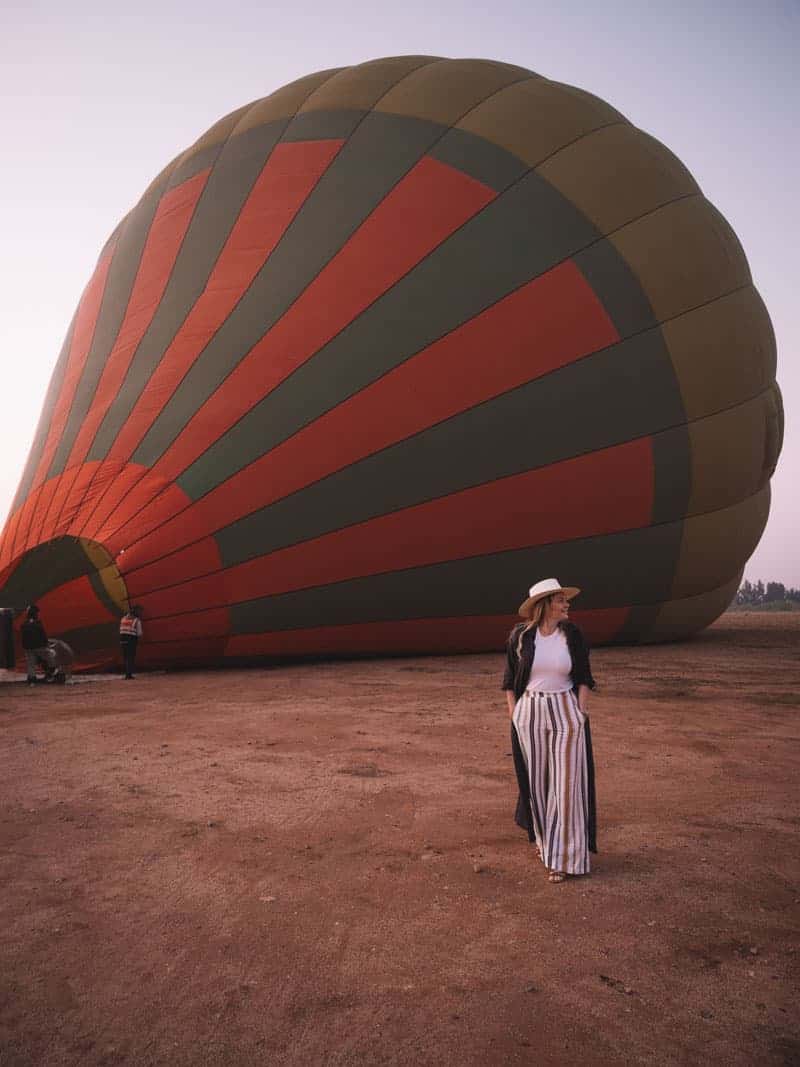Ready to take flight in Morocco: A stylish girl wanders in front of a hot air balloon being filled with air.