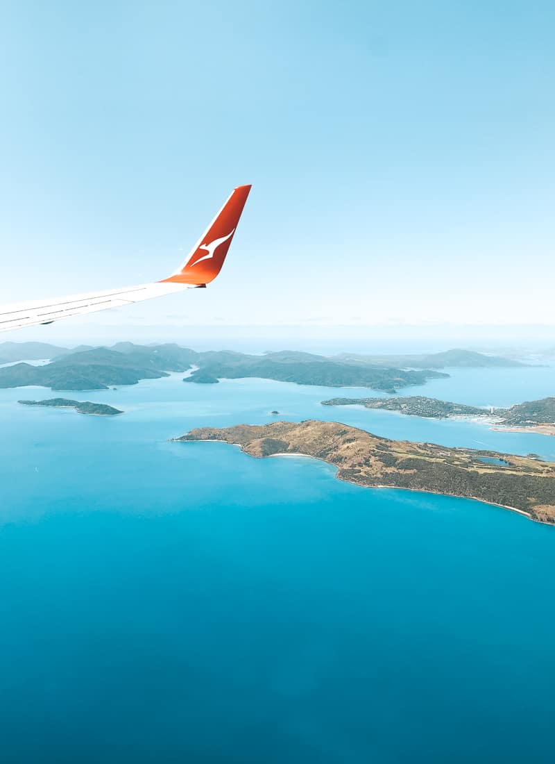 Qantas winglet in the blue sky with views of the Whitsunday islands below and the deep blue ocean and reef