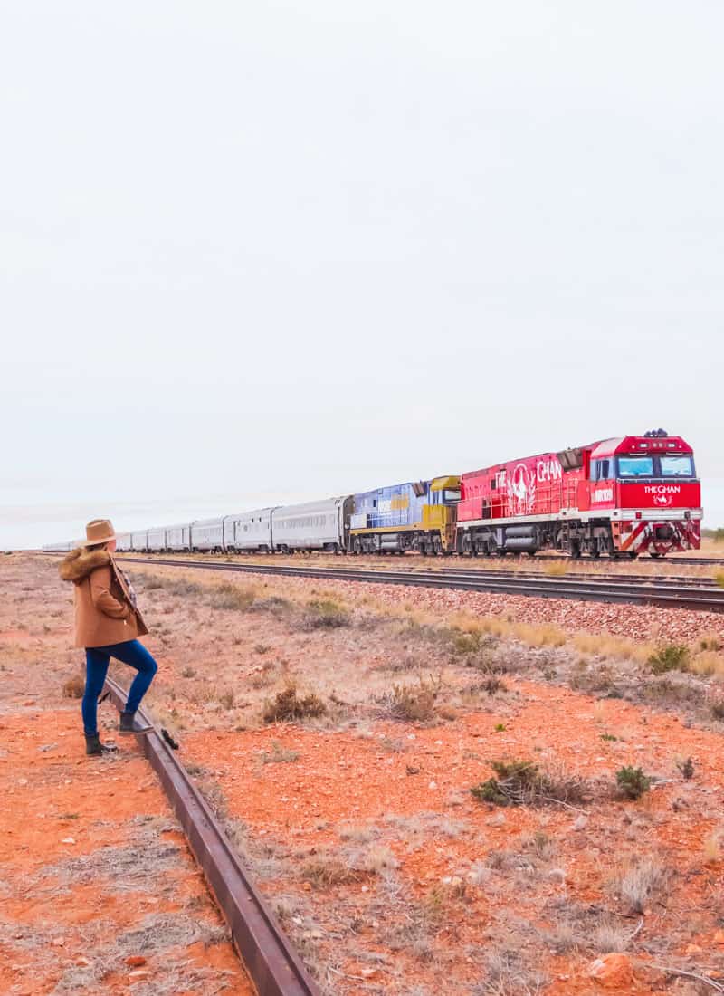 Girl standing on the railway tracks looking at the Ghan train red engine. The train stretches on for miles through the desert