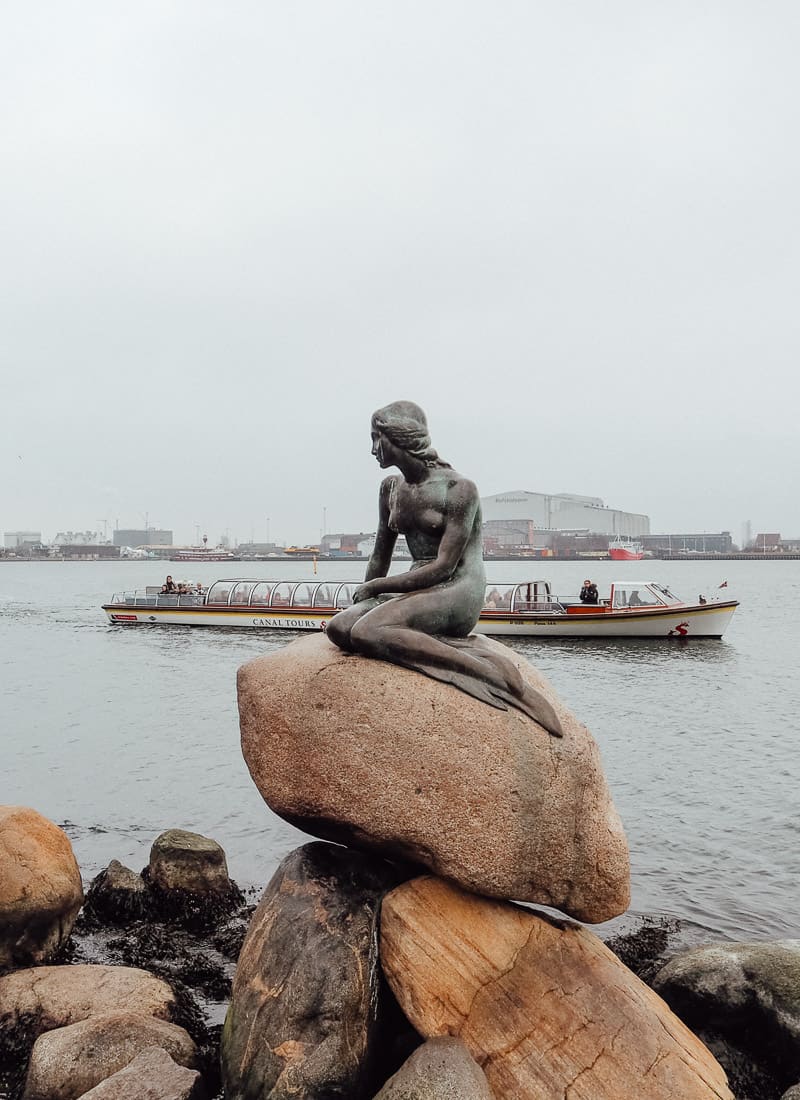The Little Mermaid Statue in Copenhagen with a canal boat in the background